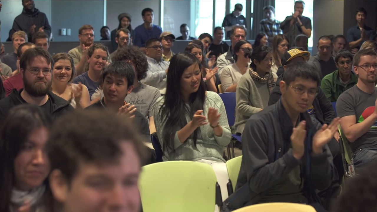 Diverse audience clapping during Google Talks presentation.