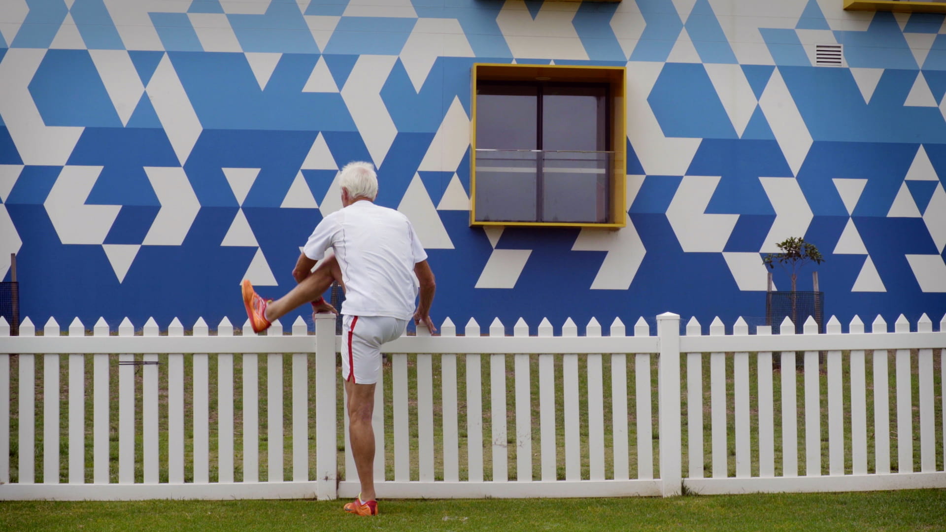 Older man stretches against a white picket fence.