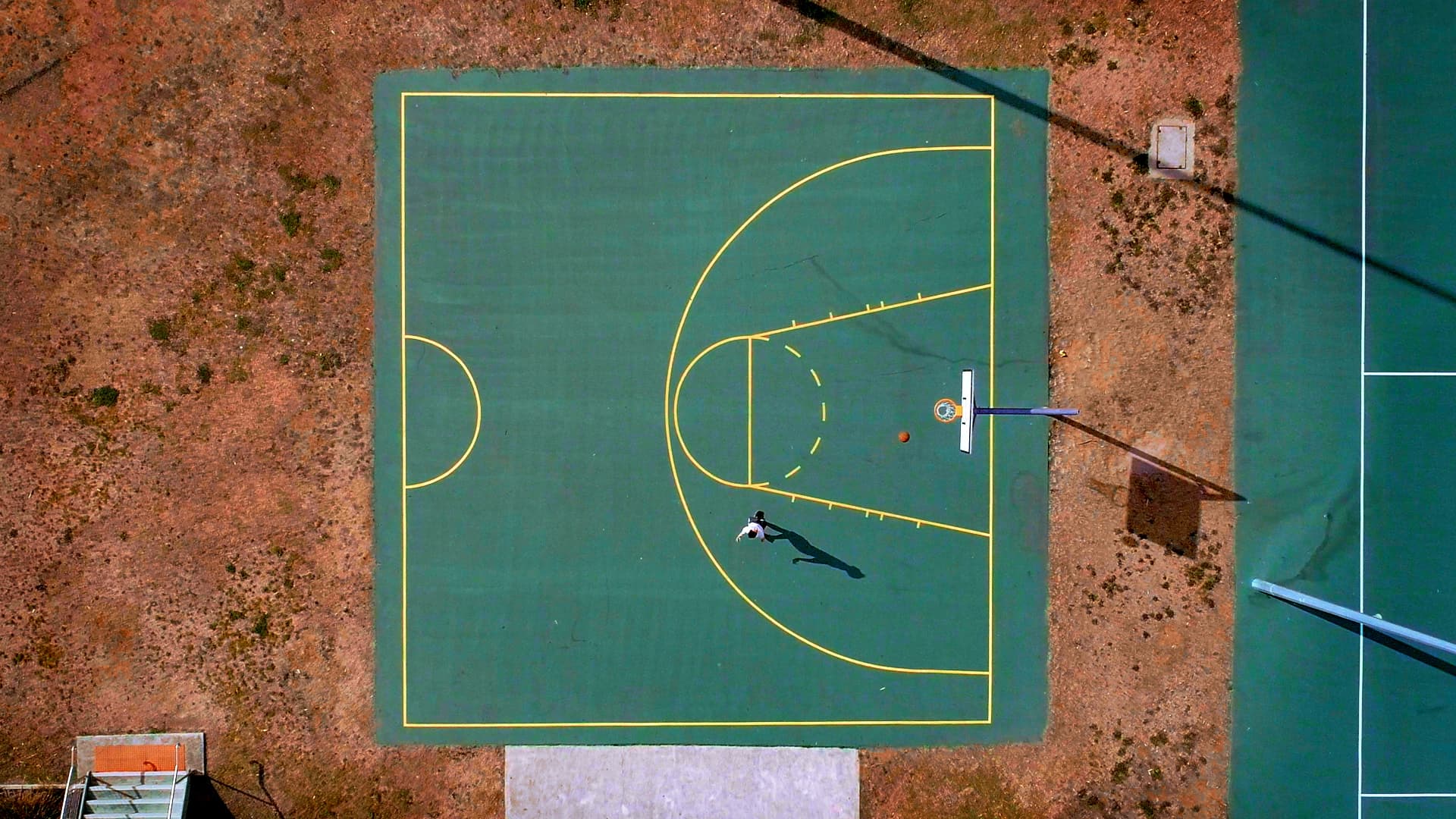 Aerial top-down shot of lone person on a basketball half-court shooting hoops.