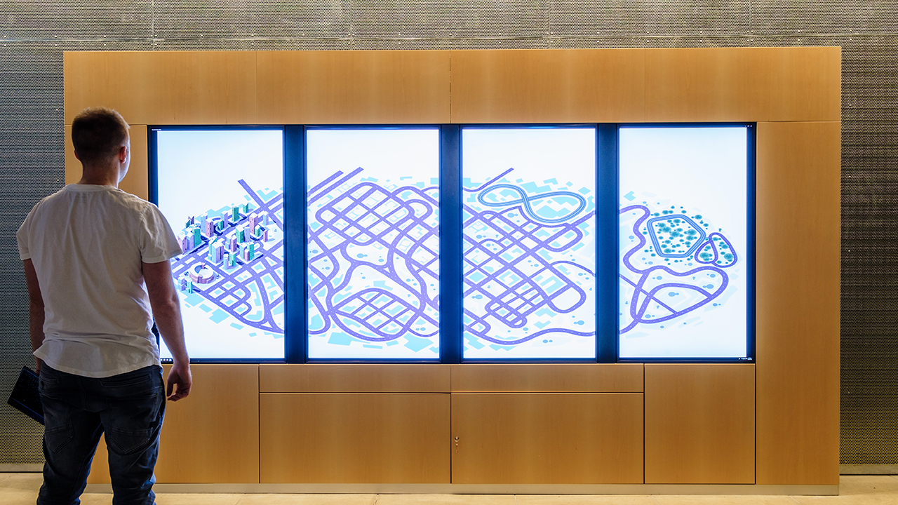 Wideshot of Road to Zero foyer activation, four vertical screens displaying a large stylised cityscape.