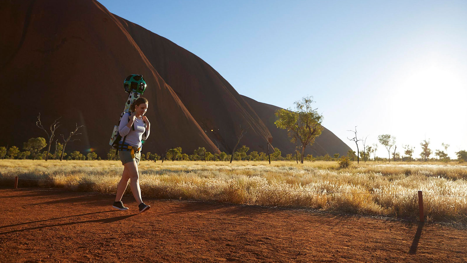 Woman on dirt track with Uluru in background.